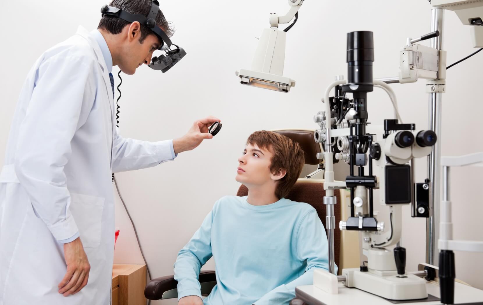 A patient sitting in a chair looks up as their optometrist examines the back of their eye during an eye dilation.