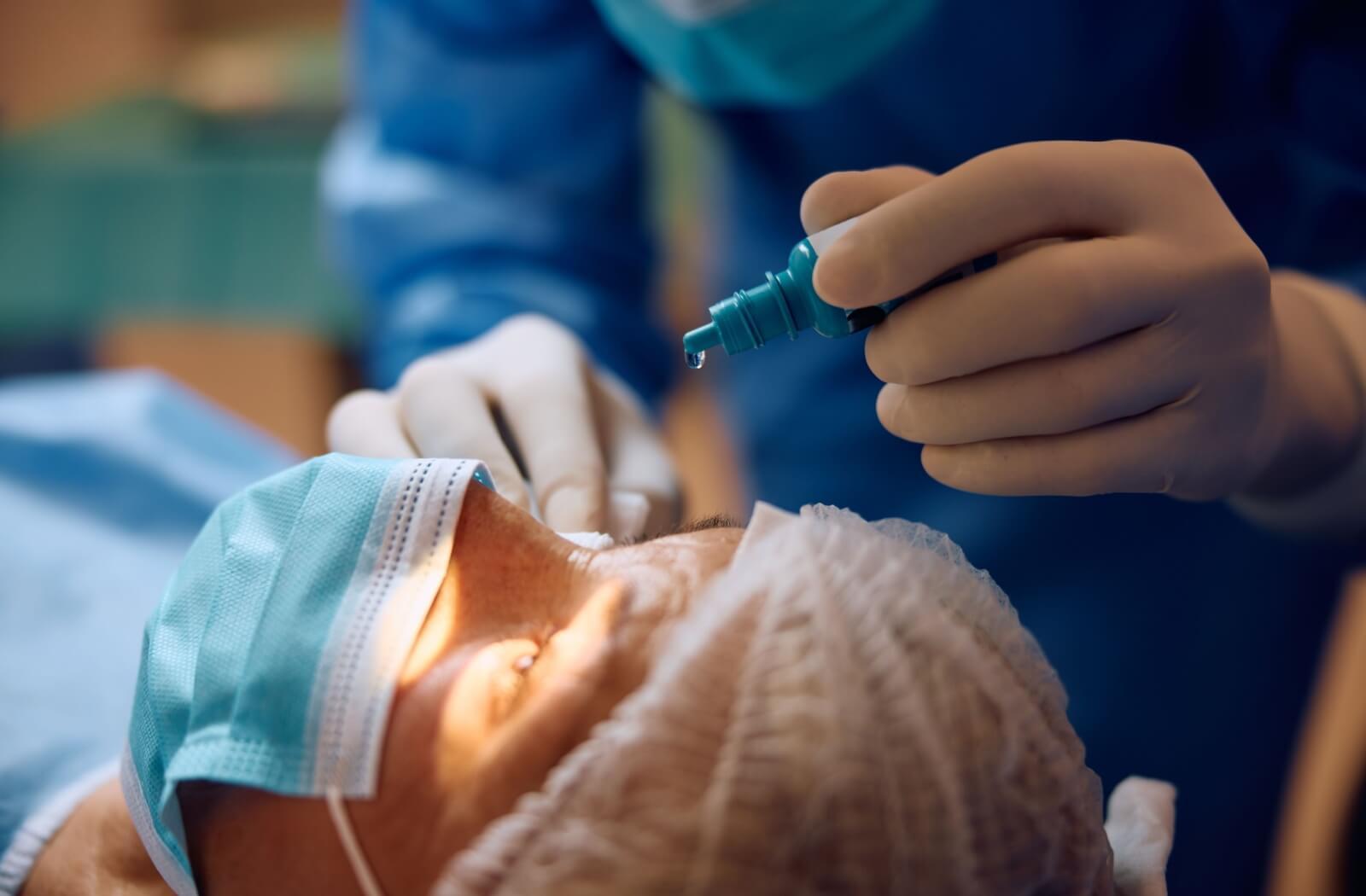 A surgeon prepares a patient for cataract surgery by administering specialty eye drops.
