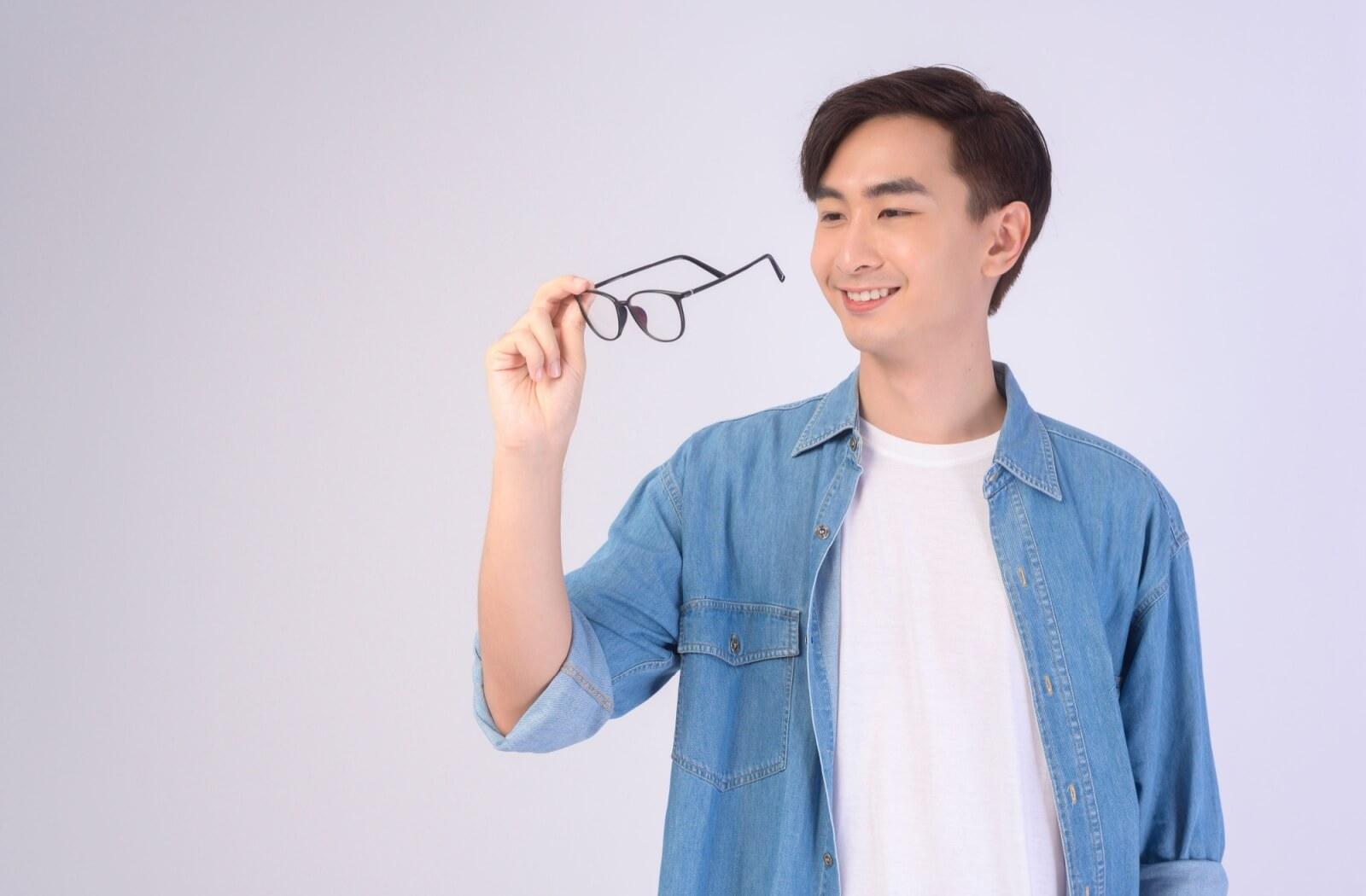 Smiling man holding glasses, celebrating freedom from glasses after LASIK.